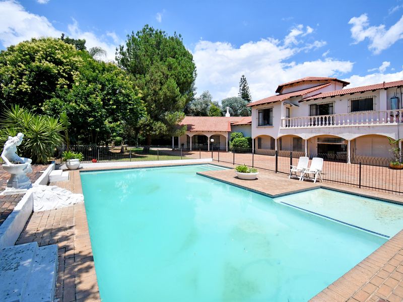 Spacious outdoor pool area featuring a large swimming pool, brick paving, and a two-story residence with a balcony and classic architectural arches.