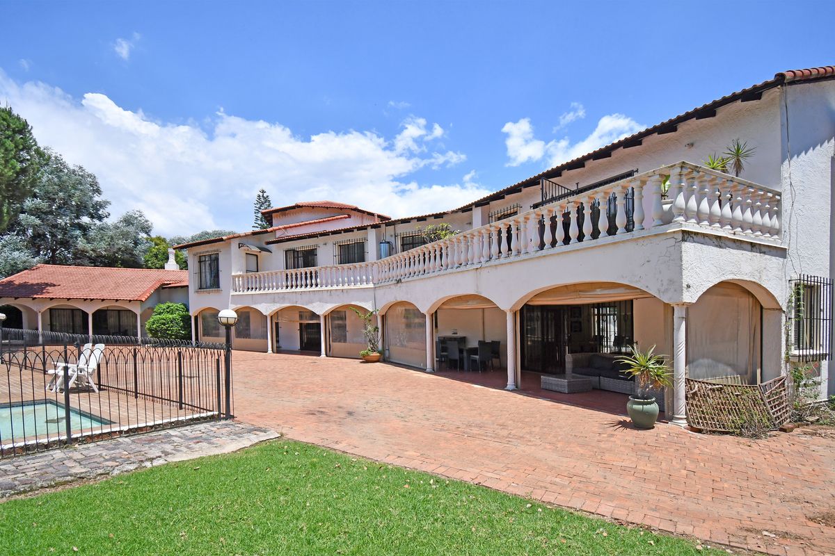 Spacious rear exterior featuring a large terracotta patio, swimming pool with iron fencing, and an expansive covered veranda with a balcony above.