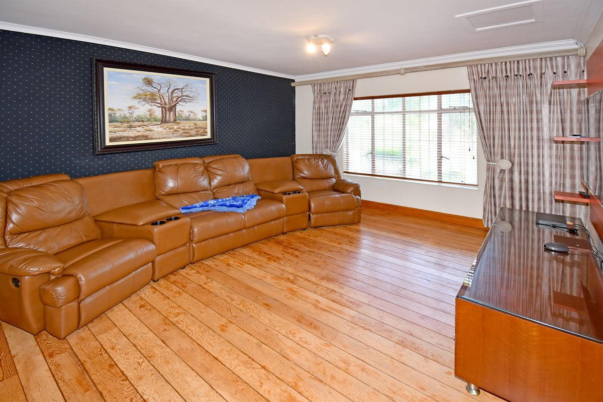 A living room featuring timber flooring, a dark feature wall, and large windows with fitted blinds and curtains.