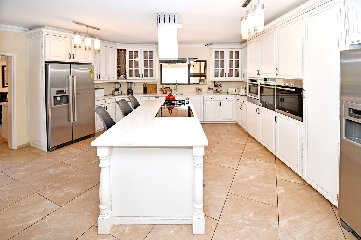 Spacious kitchen featuring a large central island with a gas cooktop, ample white cabinetry, stone countertops, and integrated double ovens.