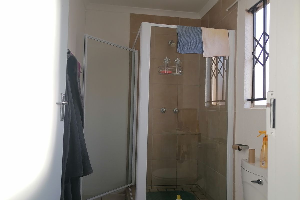 A functional bathroom featuring a glass-enclosed shower, tiled walls, and a standard toilet with security bars on the window.