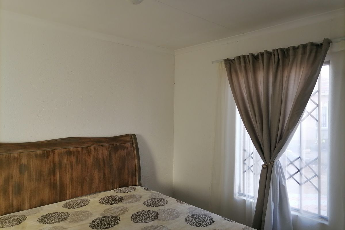 A simple bedroom featuring a window with security bars and neutral wall finishes.