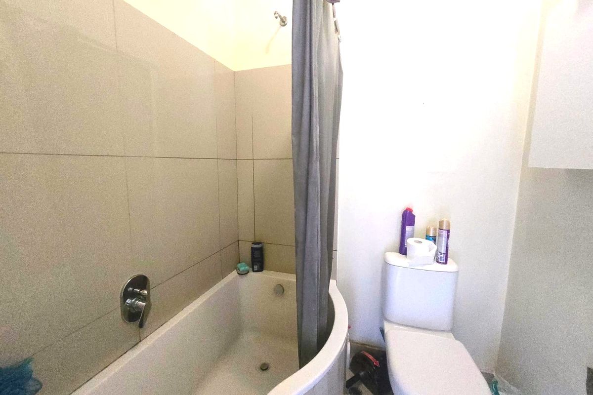 A functional bathroom featuring a bathtub with shower mixer, wall tiling, and a standard toilet.