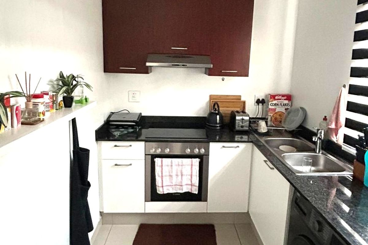 Compact kitchen featuring dark and white cabinetry, granite countertops, integrated oven and hob, and a built-in washing machine.