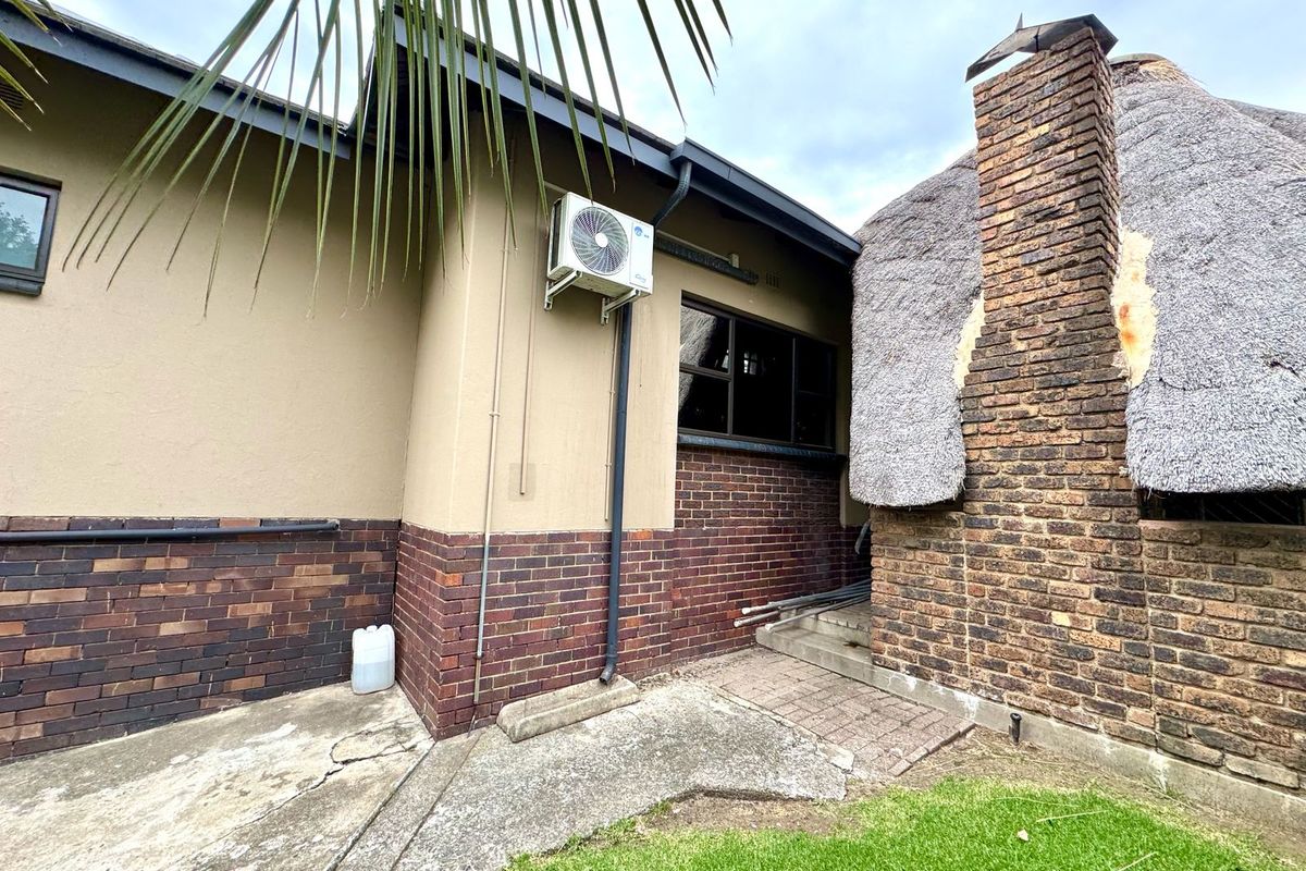Rear exterior view showing a brick chimney, thatched roof section, and concrete paving with an installed air conditioning unit.