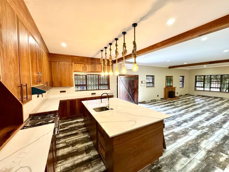 Spacious open-plan kitchen and living area featuring a large island with quartz countertops, wooden cabinetry, and a fireplace, finished with modern tiled flooring.