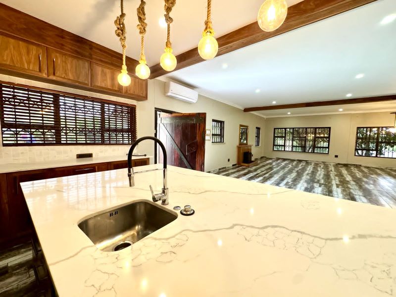 Spacious open-plan living area featuring a modern kitchen island with quartz countertops, exposed timber beams, and a fireplace in the adjoining living space.