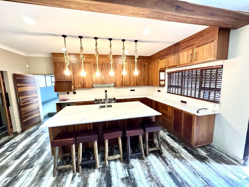 Modern kitchen featuring rich wooden cabinetry, stone countertops, a central island with seating, and integrated appliances, finished with stylish tiled flooring.