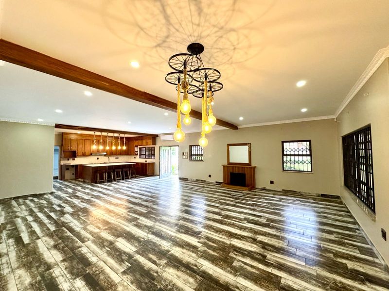 Spacious open-plan living and kitchen area featuring wood-look tiled flooring, exposed ceiling beams, a built-in fireplace, and a large kitchen island.