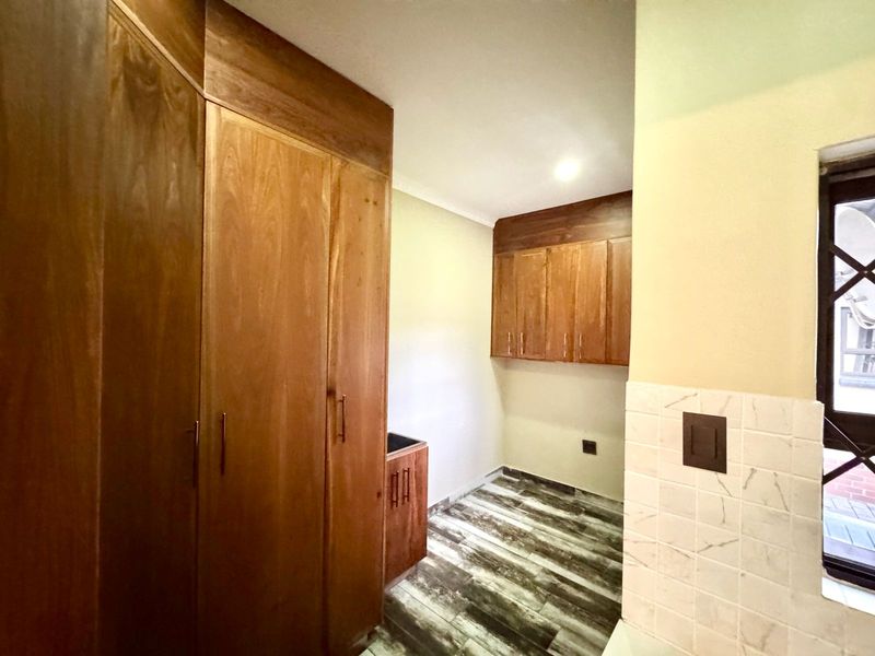 A clean and functional scullery area featuring extensive built-in wooden cabinetry, modern wood-look flooring, and marble-style wall tiling.