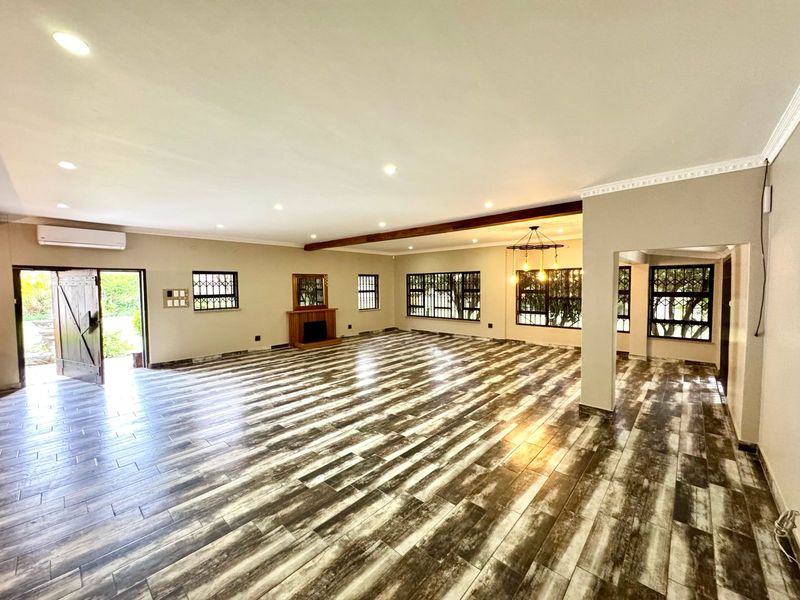 Spacious open-plan living area featuring wood-look tile flooring, a fireplace, recessed lighting, and large windows with security bars.