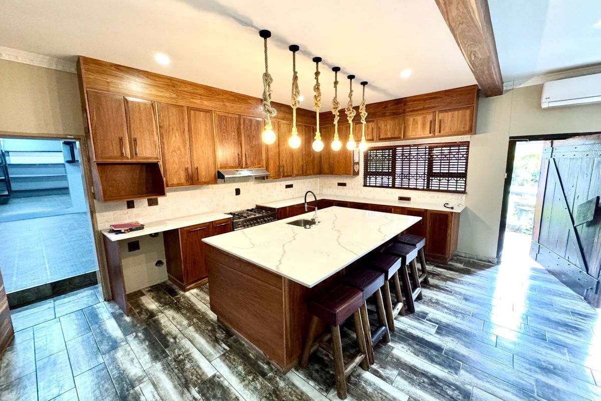Modern kitchen featuring warm wooden cabinetry, a large stone-topped island with seating, integrated appliances, and stylish pendant lighting throughout the space.