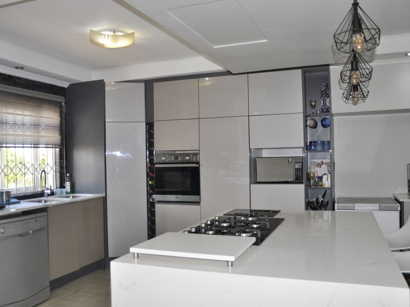 Modern kitchen featuring a central island with gas hob, stone countertops, integrated cabinetry, built-in oven, and microwave, offering a sleek and functional workspace.