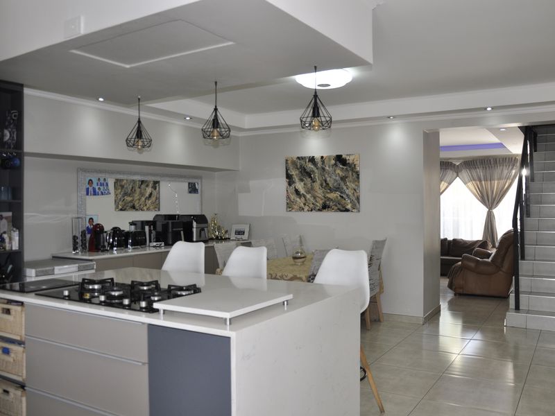 Modern open-plan kitchen featuring a central island with a gas hob, sleek cabinetry, and tiled flooring, seamlessly flowing into the dining and living areas.