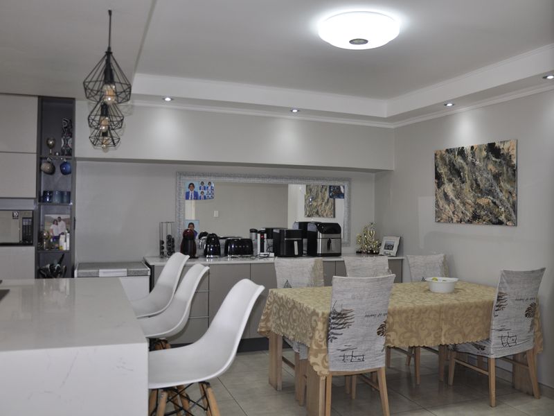 Modern open-plan kitchen and dining area featuring a stone-topped island, sleek cabinetry, recessed lighting, and neutral tiled flooring.