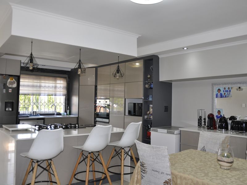 Modern open-plan kitchen featuring a central island with gas hob, sleek cabinetry, integrated shelving, and contemporary pendant lighting, seamlessly connecting to the dining area.