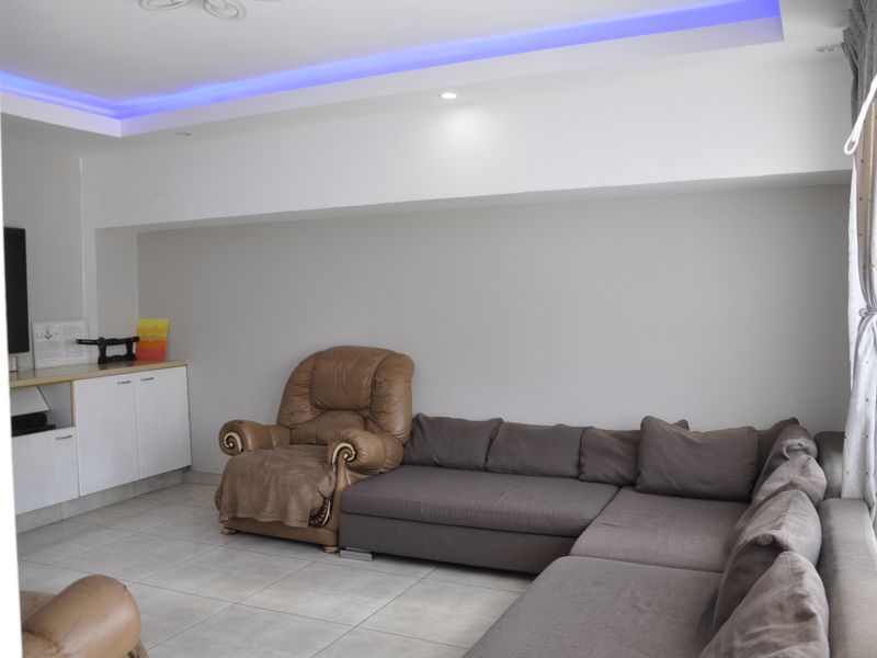 A living room featuring tiled flooring, built-in cabinetry, and recessed ceiling lighting with integrated ambient blue accent lighting.