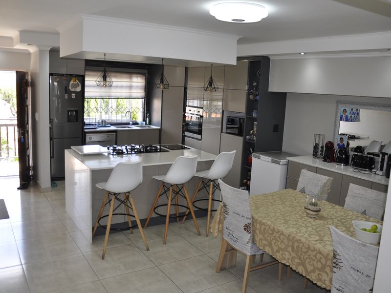 Modern open-plan kitchen and dining area featuring a central island with gas hob, sleek cabinetry, built-in appliances, and neutral tiled flooring.