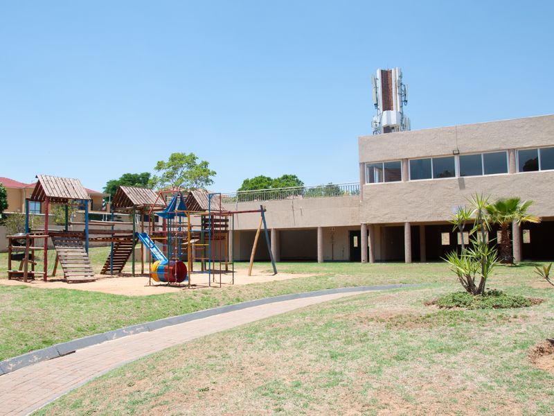 Rear exterior view of the apartment complex featuring a communal lawn, playground equipment, and a covered patio area.