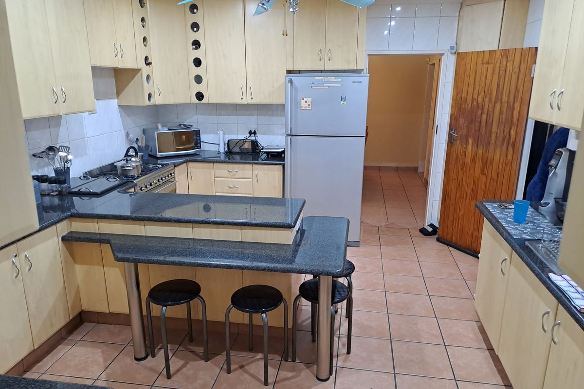 A functional kitchen featuring light wood cabinetry, dark granite countertops, a breakfast bar, and tiled flooring with direct access to an adjacent hallway.