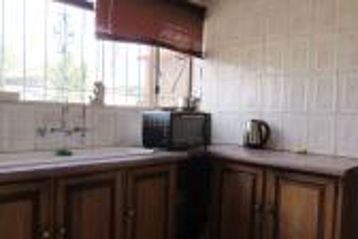 A functional kitchen area featuring dated wooden cabinetry, laminate countertops, and a double basin sink with security bars on the window.