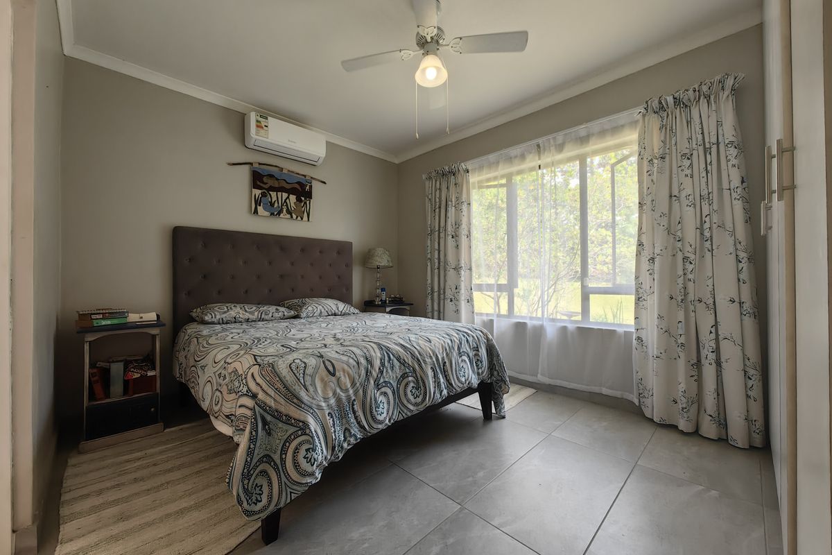 A well-maintained bedroom featuring tiled flooring, a ceiling fan, and a split-system air conditioner, offering a comfortable and functional living space.