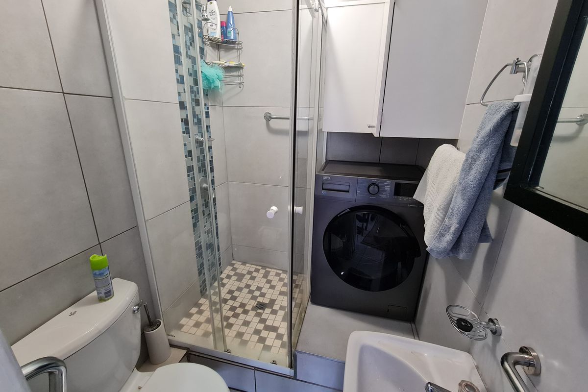 Compact bathroom featuring a glass shower enclosure, mosaic tile accents, a pedestal basin, and a built-in washing machine space.