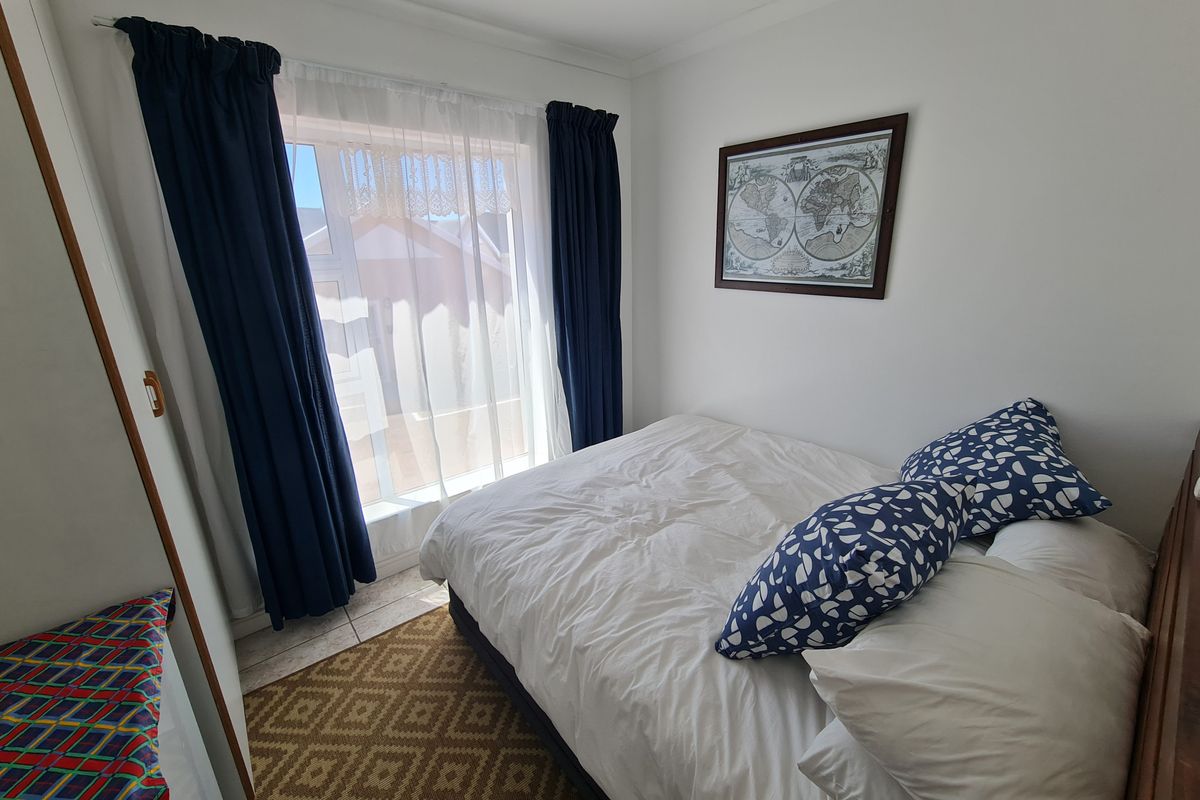 A compact bedroom featuring tiled flooring and a built-in cupboard, with natural light entering through a window.