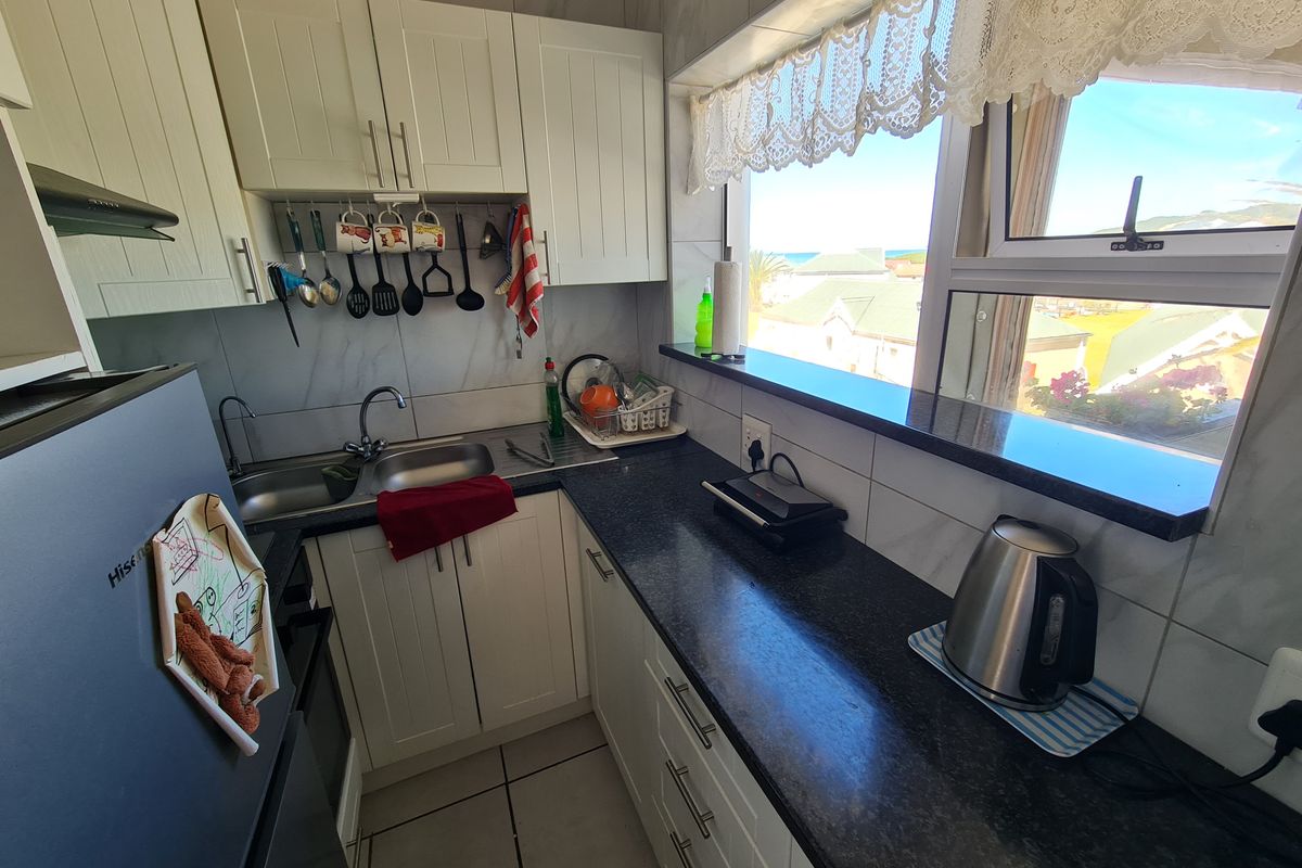 Compact kitchen featuring white cabinetry, dark granite countertops, double sink, and tiled finishes with a window overlooking the exterior.