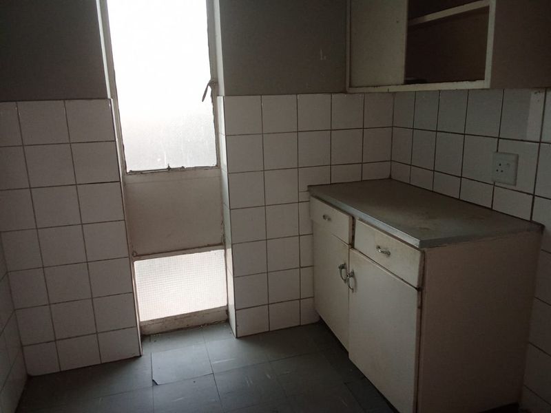 A dated kitchen area featuring original built-in cabinetry, tiled splashbacks, and a window, offering a blank canvas for a modern renovation.