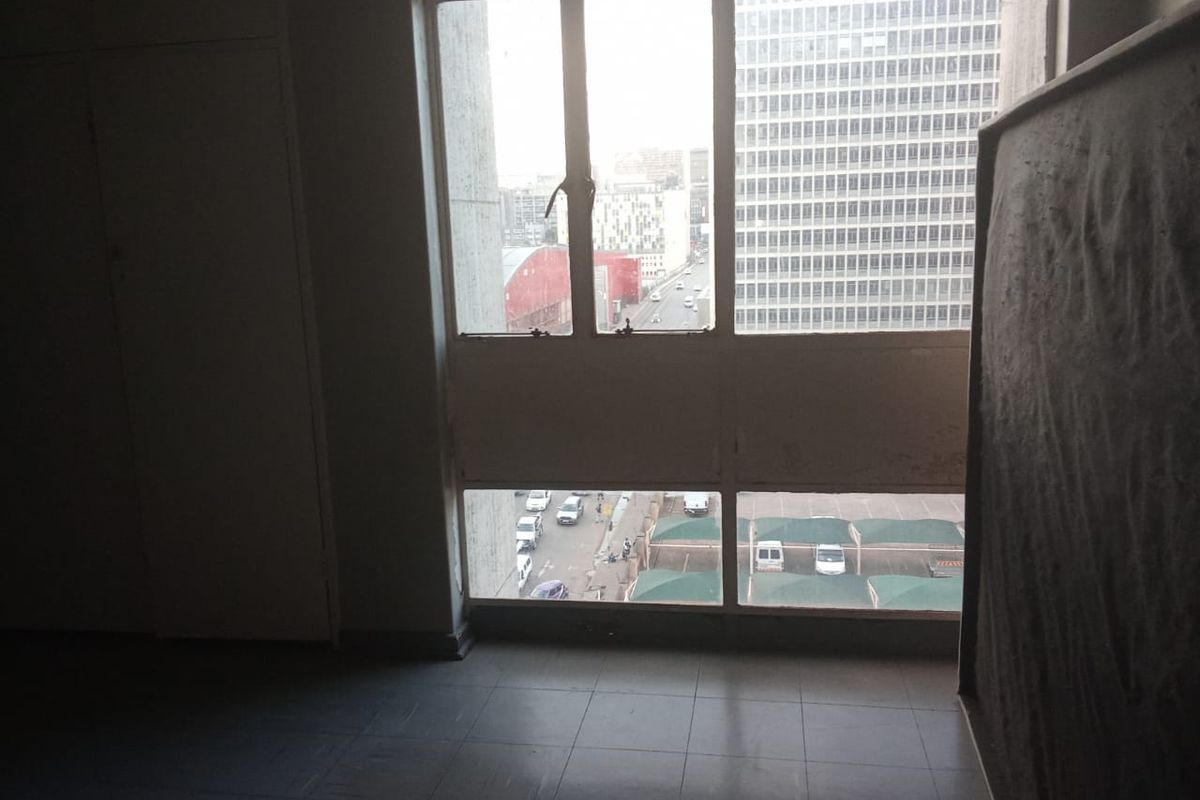 An empty bedroom featuring tiled flooring, built-in cupboards, and large windows offering an urban city view.