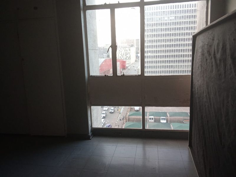 An empty bedroom featuring tiled flooring, built-in cupboards, and large windows offering an urban city view.