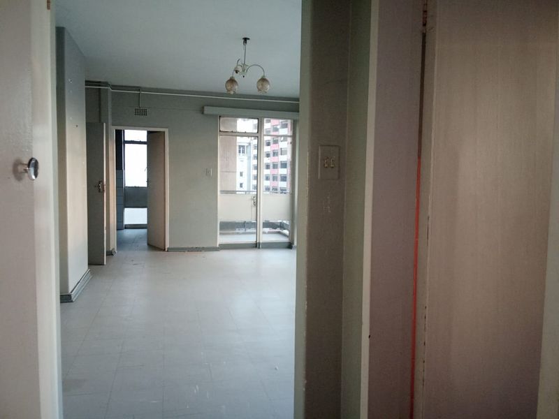 An empty, open-plan living area featuring tiled flooring and access to a balcony, presenting a blank canvas for renovation and interior design.
