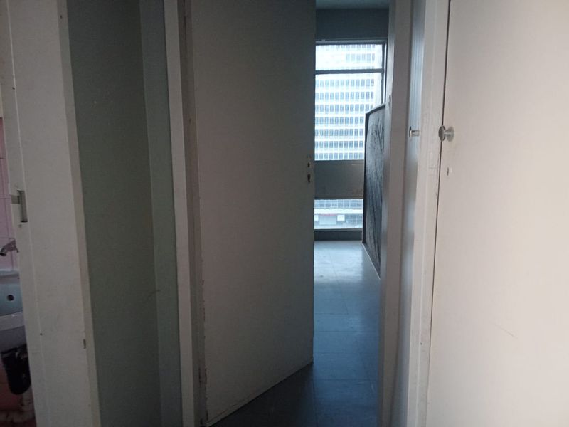A narrow interior hallway featuring built-in storage cupboards and access to adjacent rooms, showing signs of wear and requiring cosmetic updates.