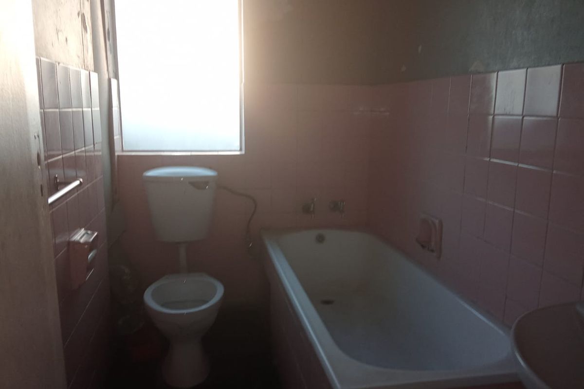 A dated bathroom featuring a bathtub, toilet, and pink wall tiles, requiring renovation to update the finishes and improve the overall condition.