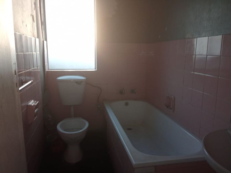 A dated bathroom featuring a bathtub, toilet, and pink wall tiles, requiring renovation to update the finishes and improve the overall condition.