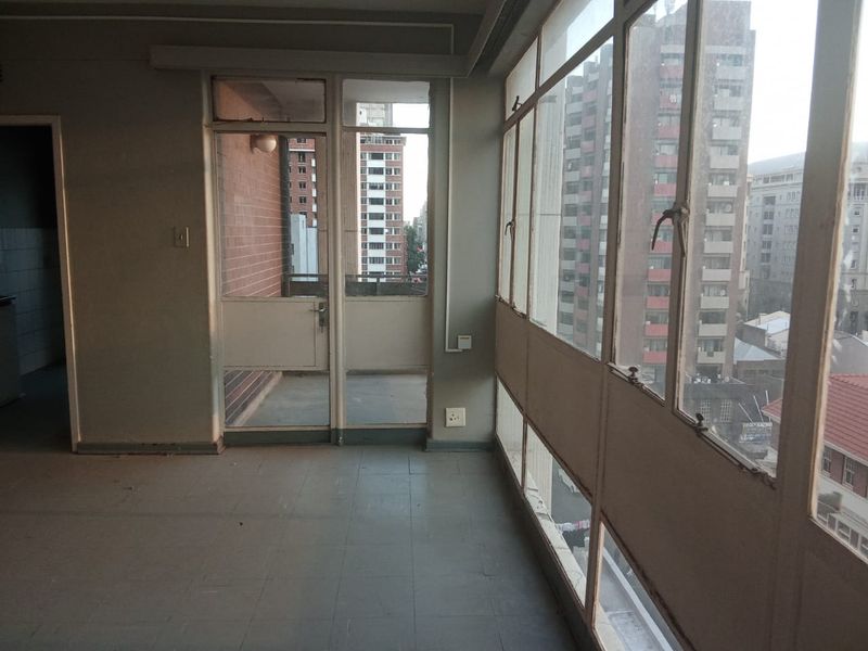 An enclosed balcony area featuring tiled flooring and large metal-framed windows with urban views, offering a versatile space for renovation.