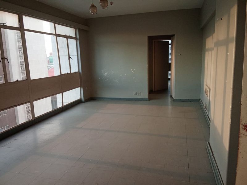 An empty, sunlit living area featuring large windows and tiled flooring, requiring cosmetic updates to restore its appeal.