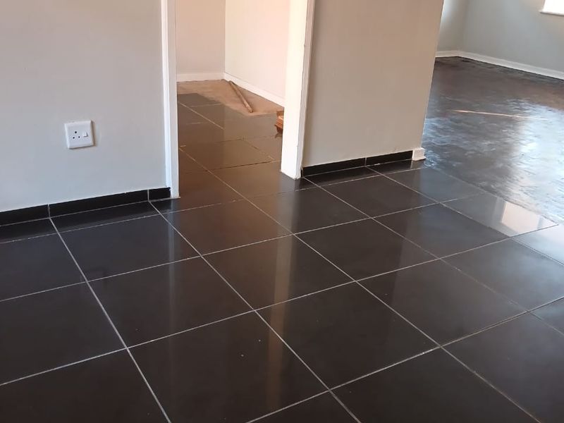 An empty open-plan living area featuring dark tiled flooring and neutral wall finishes, currently undergoing renovation or flooring installation.
