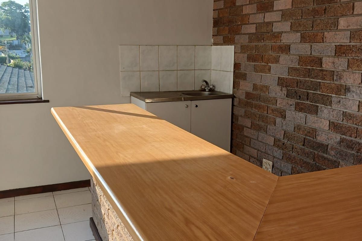 A compact kitchen area featuring a built-in breakfast bar, exposed brick wall, and tiled flooring, offering a functional space ready for modernization.