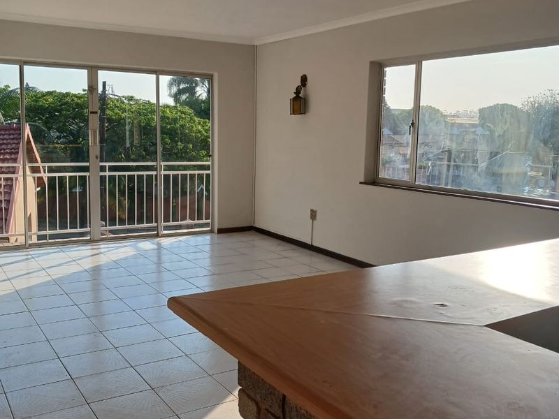 Spacious open-plan living area featuring tiled flooring, a brick breakfast bar, and large windows providing ample natural light and access to a balcony.