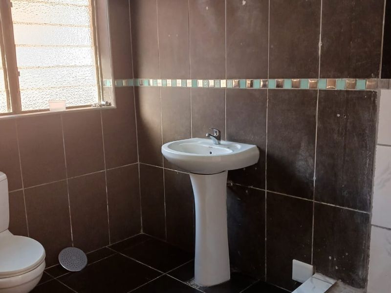 A functional bathroom featuring dark wall and floor tiles, a pedestal basin, toilet, and a tiled shower base.