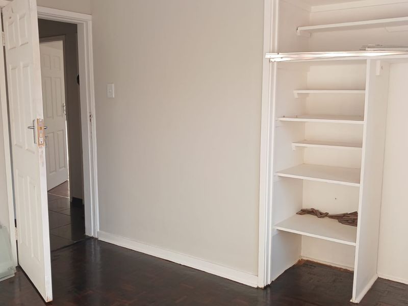An empty bedroom featuring classic parquet flooring and a built-in storage cupboard with shelving.