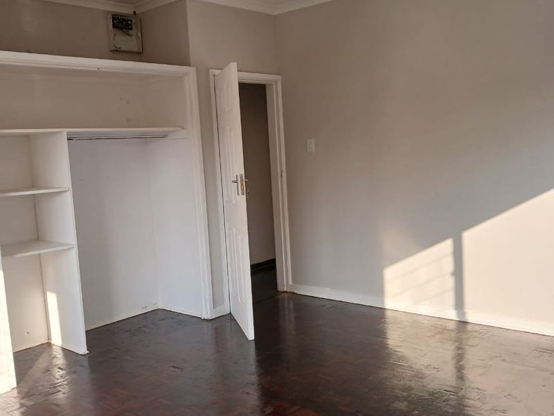 An empty bedroom featuring dark parquet flooring, a built-in wardrobe, and a coved ceiling, providing a blank canvas for interior design.