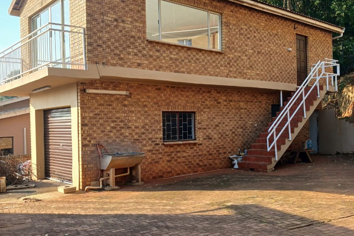 Rear view of a two-story face brick house featuring an external staircase, balcony, garage, and paved driveway area.
