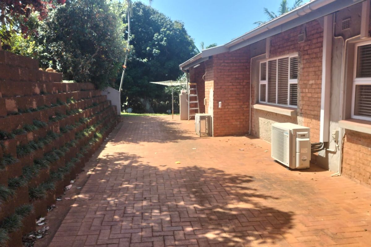 Rear exterior area featuring brick paving, a retaining wall, and an external air conditioning unit against the brick house facade.