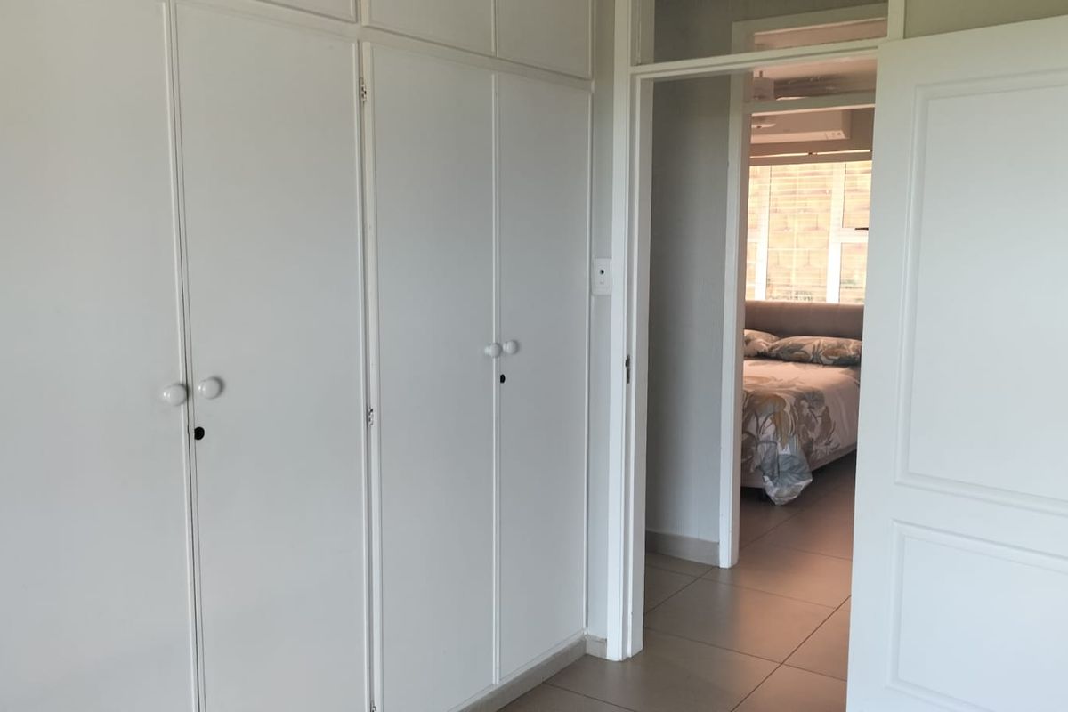 A bedroom featuring white built-in cupboards and tiled flooring, with a view into an adjacent bedroom space.