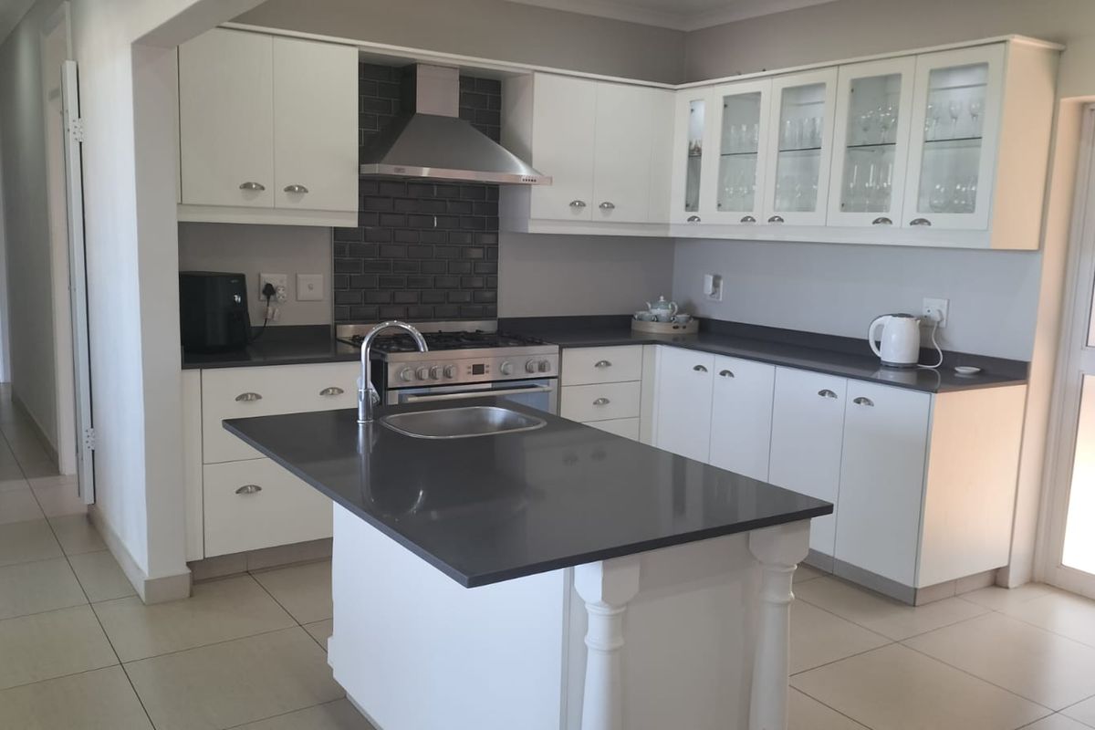Modern kitchen featuring white cabinetry, dark stone countertops, a central island with a sink, and a stainless steel gas stove with extractor fan.