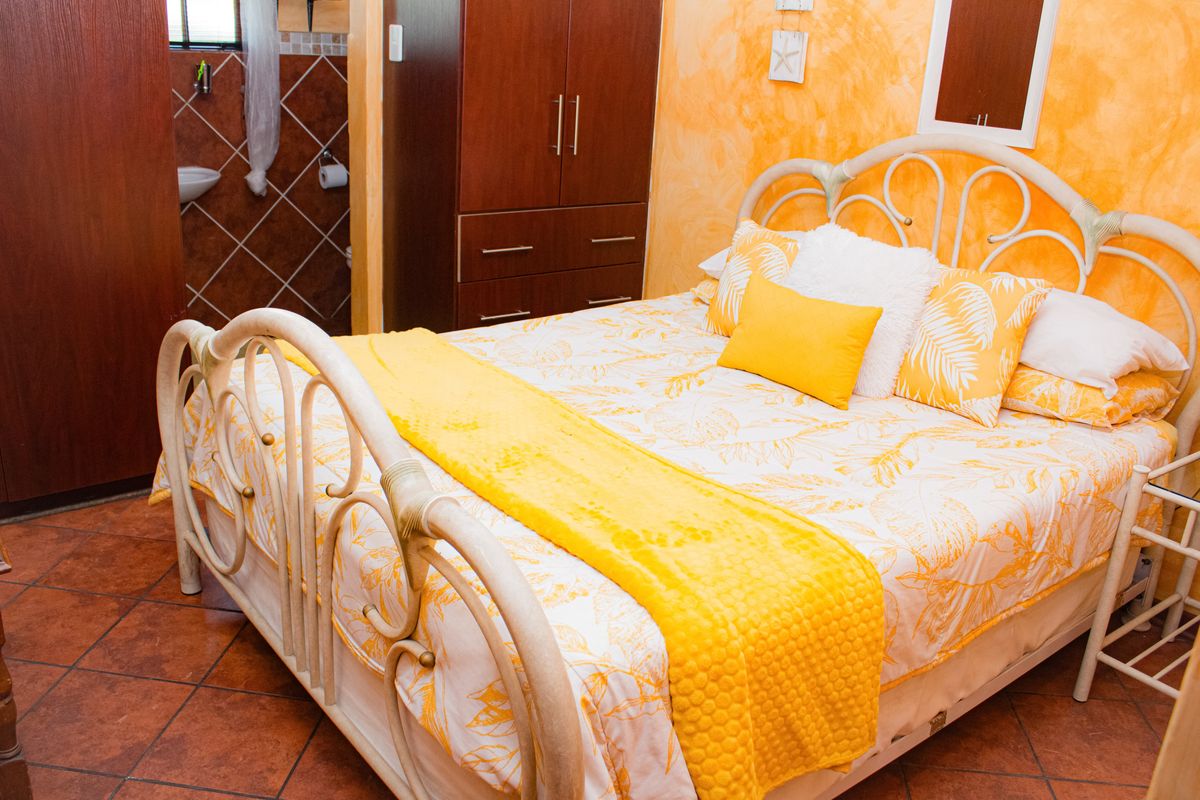 A bedroom featuring terracotta floor tiles, textured orange wall finishes, and an integrated en-suite bathroom area.
