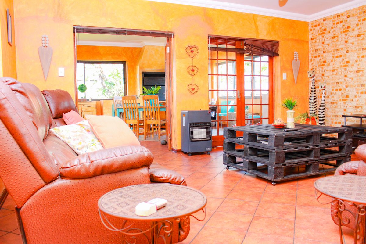 Spacious living area featuring warm-toned textured walls, exposed brick accents, and tiled flooring, with direct access to an adjoining dining space and patio.